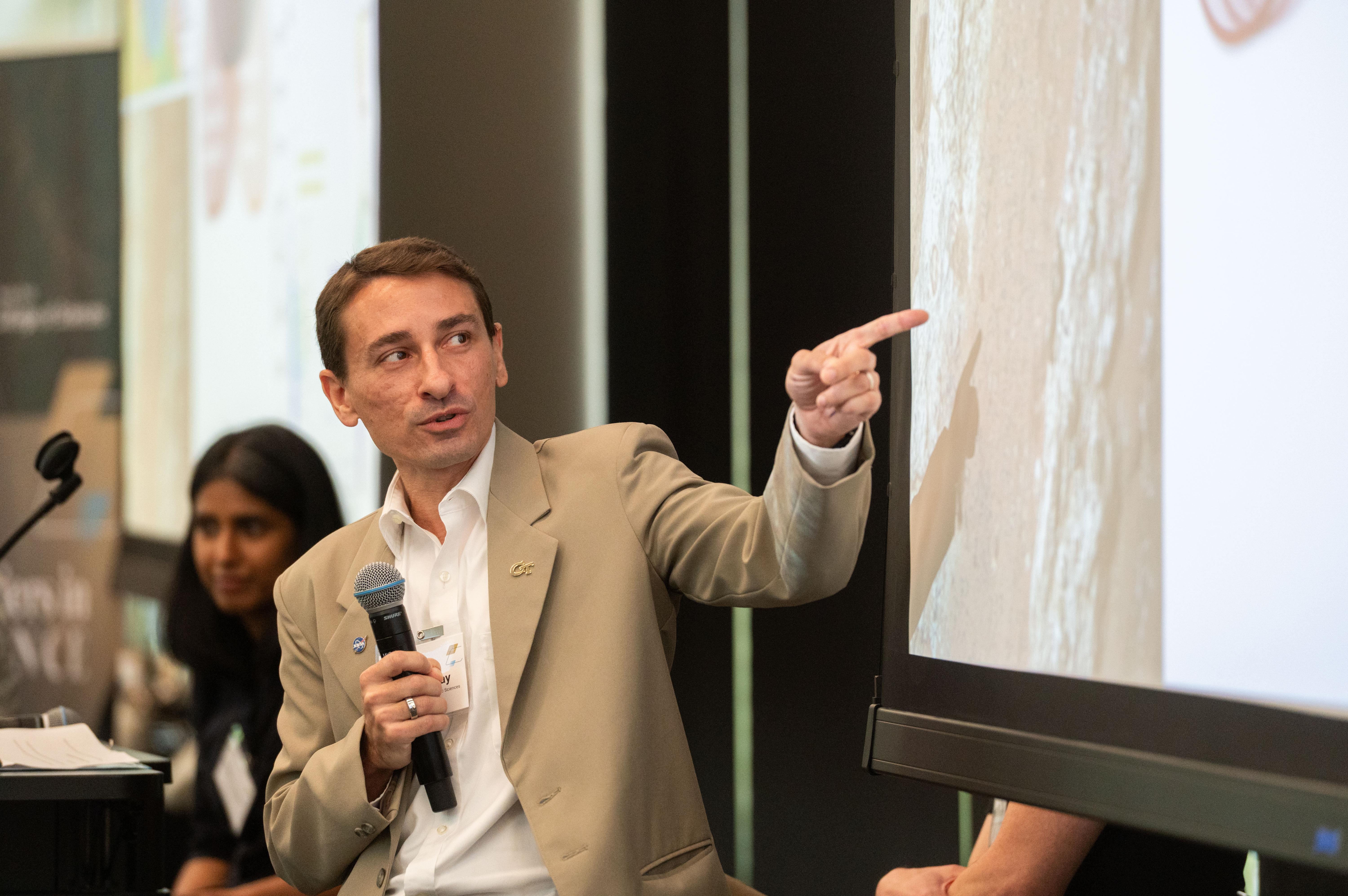 Professor James Wray holds microphone and points to powerpoint slide during his presentation