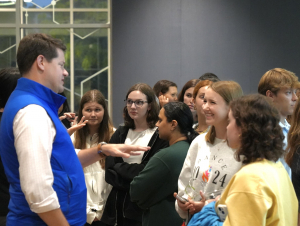 Man in blue vest speaks with students.