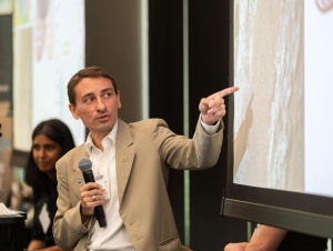 Professor James Wray holds microphone and points to powerpoint slide during his presentation