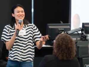 Joyce Shi Sim holds a microphone and laser pointer while presenting to room of people