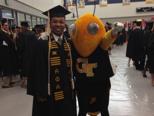 Man in graduation regalia stands with Georgia Tech mascot Buzz.