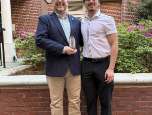 A man and a male college student shake hands and hold up an award.