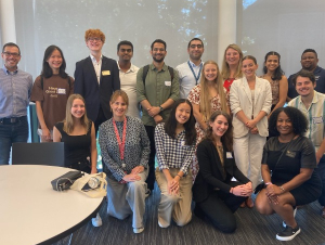 A group of students and Coca-Cola employees posing in front of a large window.