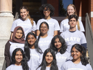 Eleven students sitting in rows in front of a brick building.